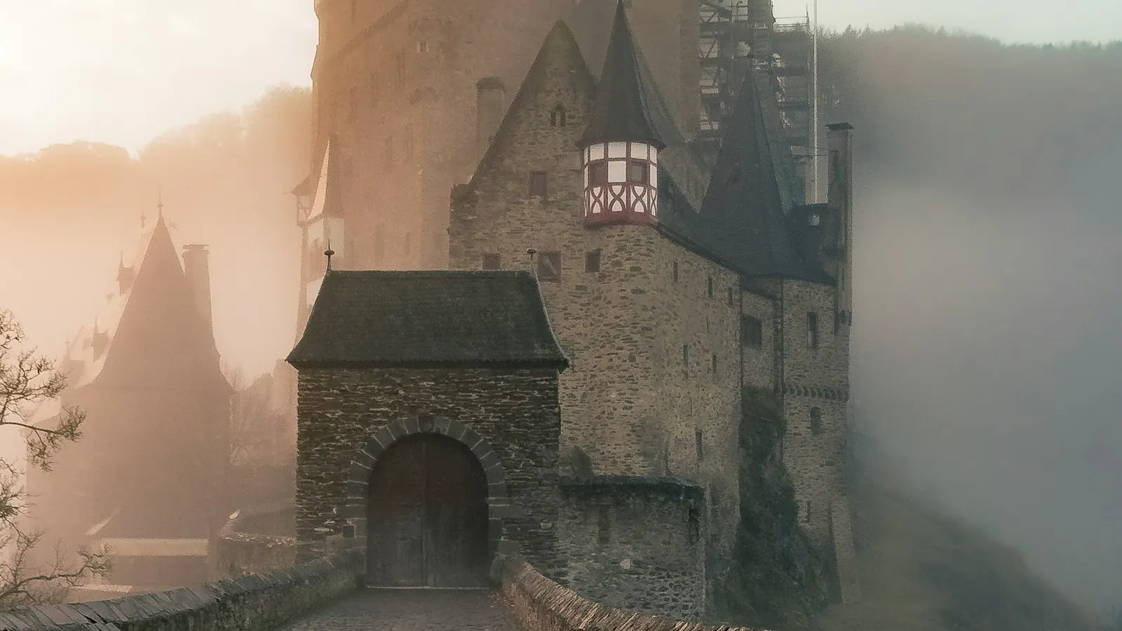 A castle in the morning mist, with the bridge to its gate